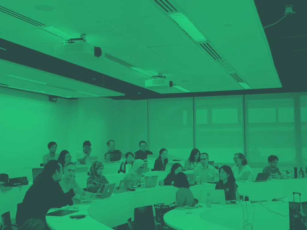Participants réunis dans une salle de formation équipée d’ordinateurs portables et de vidéoprojecteurs.